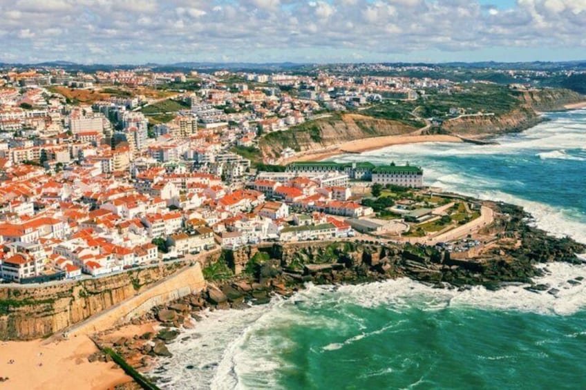 A coastal city with red-roofed buildings, a fortified structure, and a beach. 1