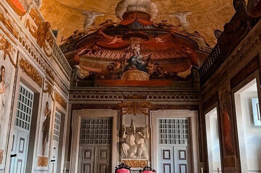 An ornate room with a high ceiling, detailed frescoes, and a central statue. 2