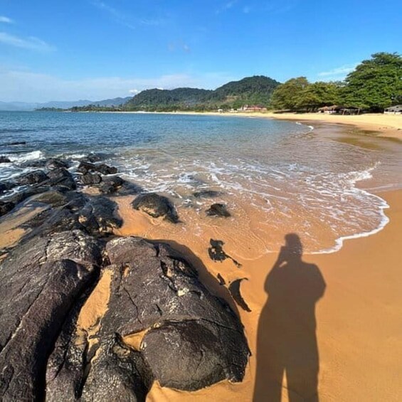 A beach with rocks, sand, and a shadow of a person. 2