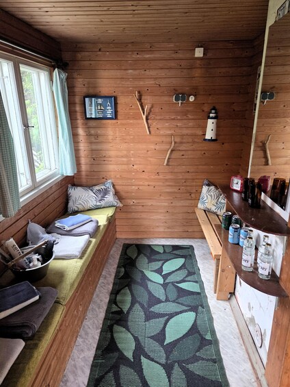 A cozy cabin interior with wooden walls, a bench, a small table with bottles, and a window with curtains. 3