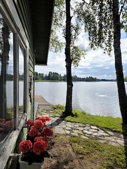 A lakeside view with a wooden dock, a row of pink flowers, and a clear sky. 1