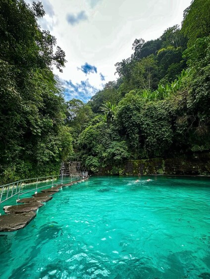 A turquoise pool surrounded by lush greenery and a stone bridge. 4