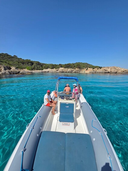 A boat with people on a clear blue sea, rocky coastline, and greenery in the background. 3