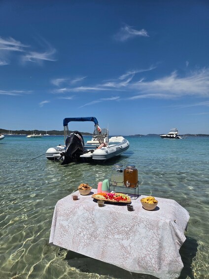 A table with food and drinks on a beach with boats in the background. 1