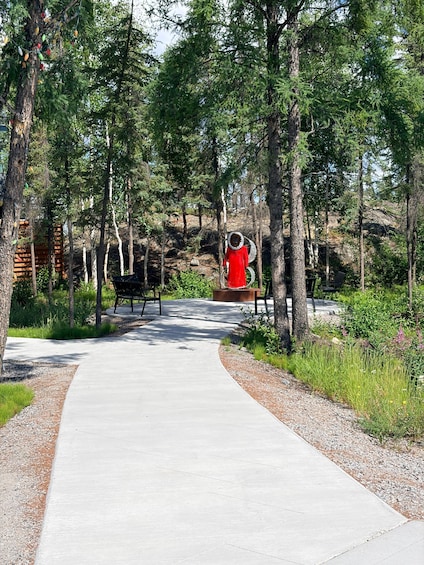A pathway through a forest with a red sculpture and benches. 4