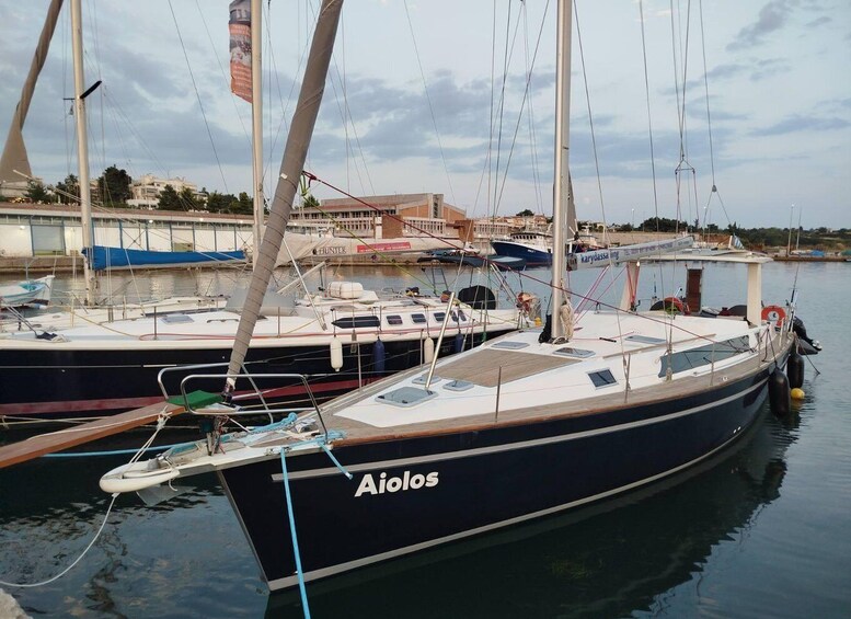 A sailboat named 'Aiolos' docked at a marina with other boats and buildings in the background. 5