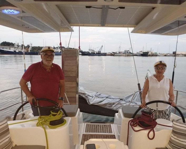 Two people on a sailboat with a marina in the background. 4