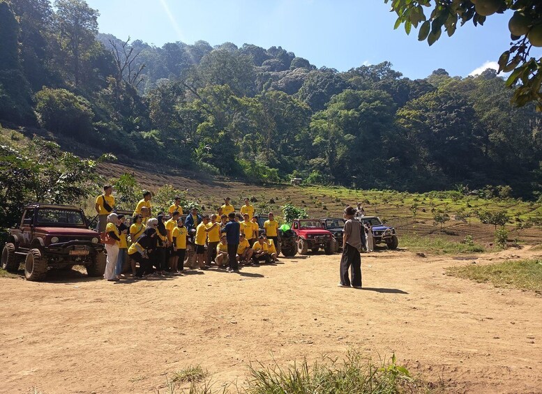 A group of people in yellow shirts gathered around off-road vehicles on a dirt road with a forested hillside in the background. 2
