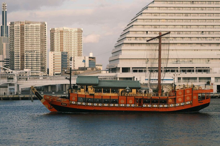 A traditional orange boat named GOZABUNE-ATAKEMARU on a river with modern buildings in the background. 4