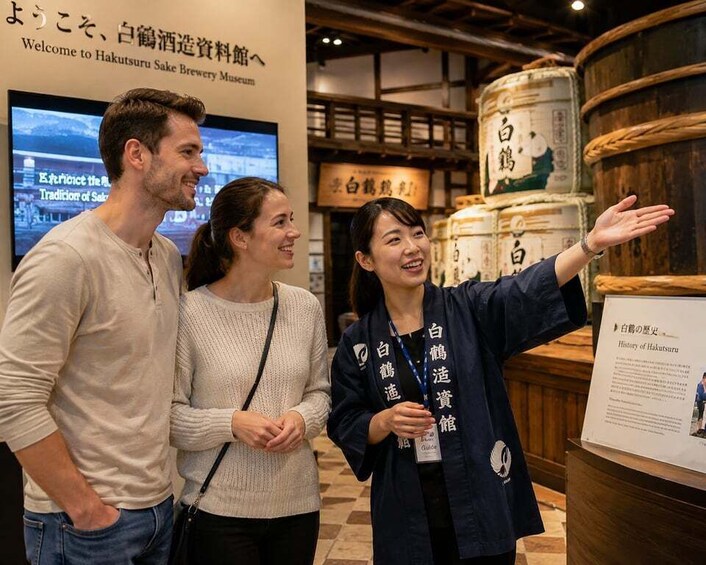 Three people at the Hakutsuru Sake Brewery Museum, with a signboard and barrels in the background. 1