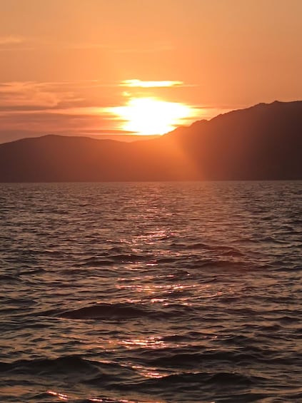 A sunset over a body of water with mountains in the background. 2