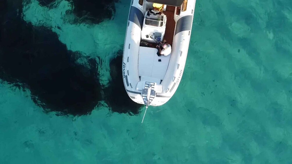 A white boat with a cabin and a motor at the stern, anchored in clear turquoise water. 5