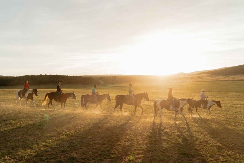 A group of people riding horses across a field during sunset. 1