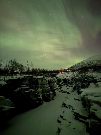 A snowy landscape with a river, ice formations, and a greenish aurora in the sky. 2