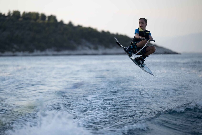 A person wakeboarding on a body of water with waves, wearing a life jacket and holding a rope. 3