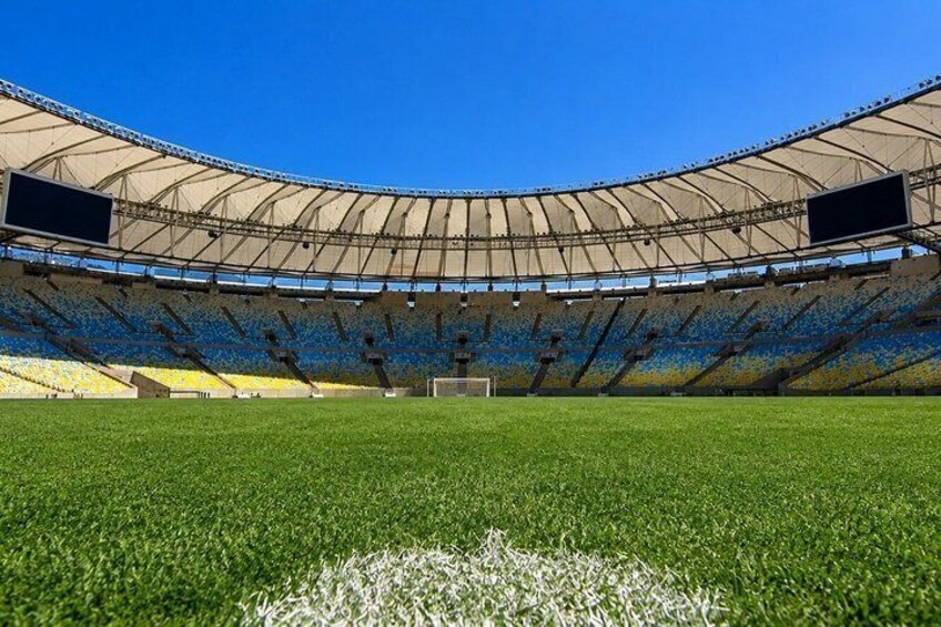 A large stadium with empty blue and yellow seats, a green field, and a clear blue sky. 2