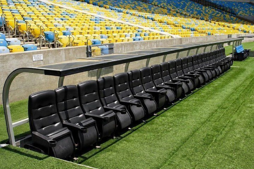 A row of black stadium seats on a green field with yellow and blue seats in the background. 3
