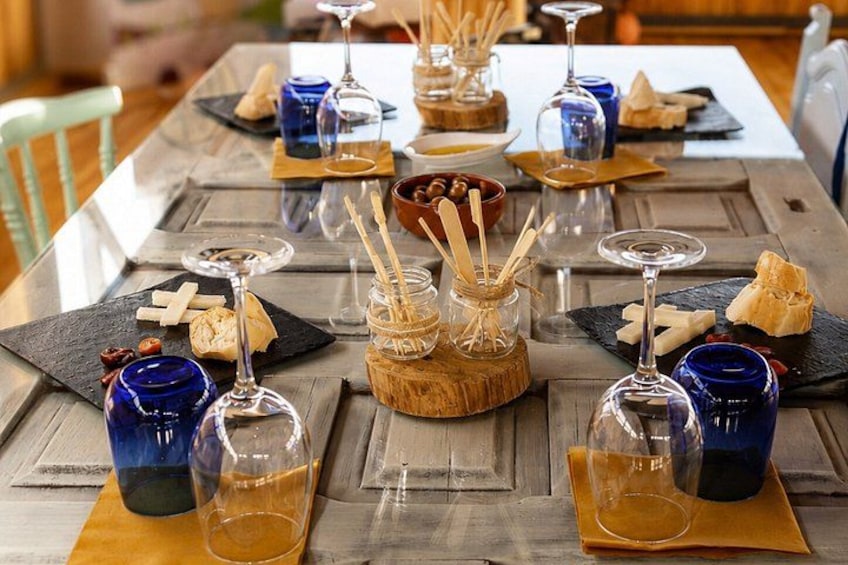 A wooden table set with blue glassware, cheese, and jars with sticks. 2