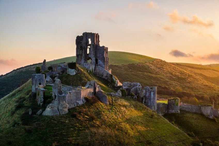 A ruined stone structure on a grassy hill with a sunset in the background. 1