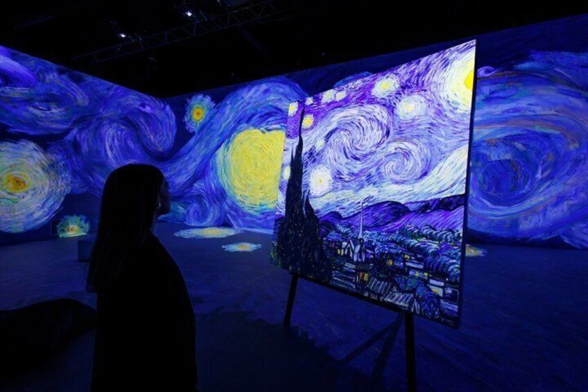 A person standing in front of a large, illuminated painting of a night sky with swirling patterns and stars. 4