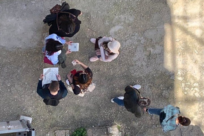 A group of people sitting on the ground outdoors, some with papers and one with a laptop. 5