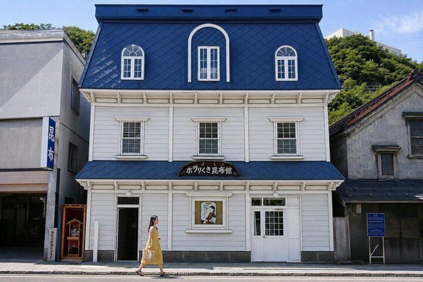 A two-story building with a blue roof and white walls, featuring a sign with Japanese characters. 2