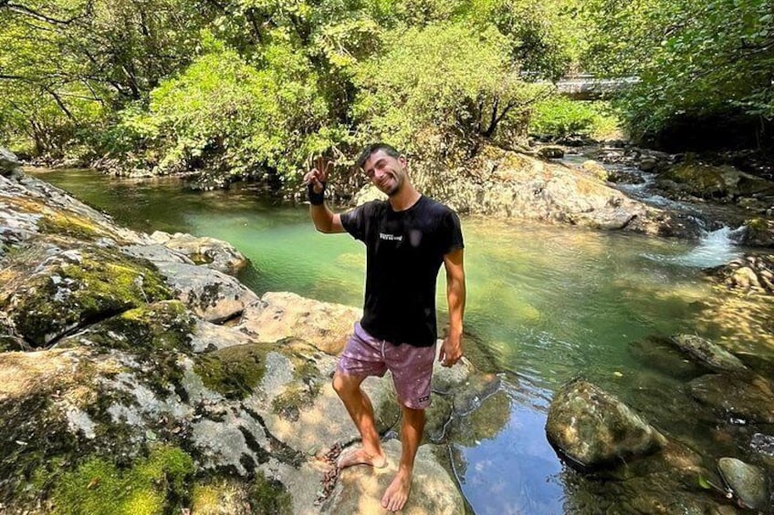 A person standing on rocks by a clear stream in a forested area. 1