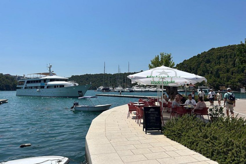 A marina with boats, a large yacht, and people dining at outdoor tables. 3