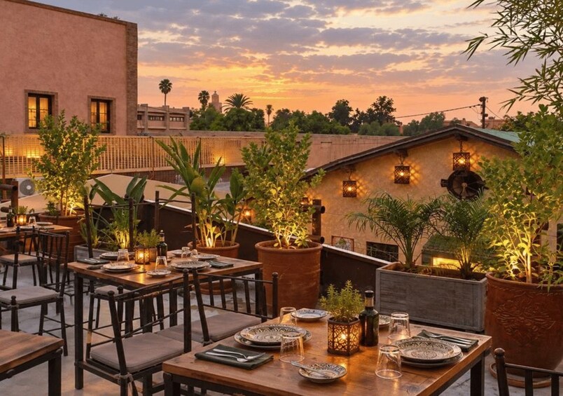 An outdoor dining area with tables and chairs, potted plants, and decorative lighting against a sunset sky. 5