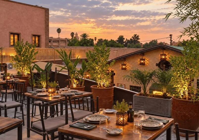 An outdoor dining area with tables and chairs, potted plants, and a sunset in the background. 2