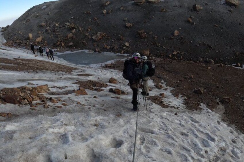 A group of hikers on a snowy trail with rocky terrain and a glacier in the background. 3
