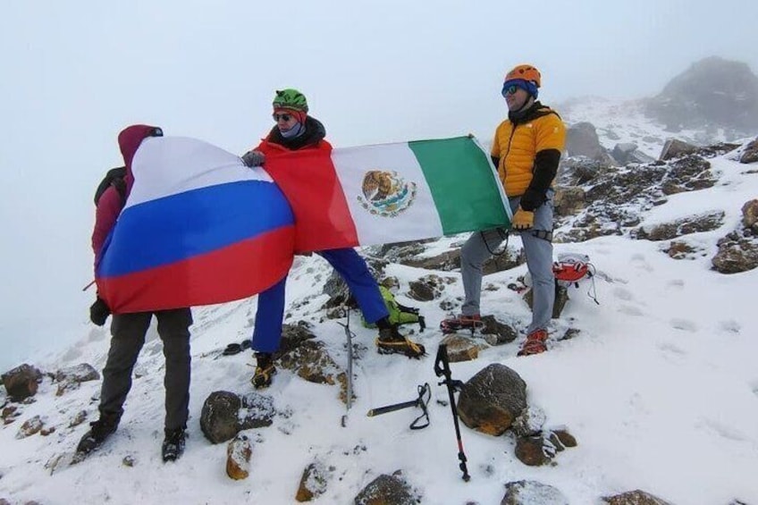 Two people holding flags on a snowy mountain peak. 5