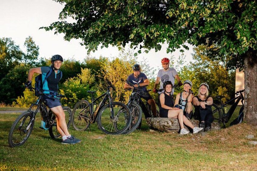 A group of cyclists resting under a tree in a grassy area. 4