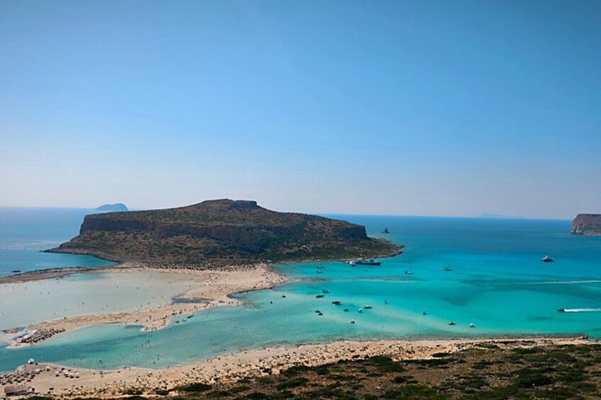 A coastal landscape with a prominent hill, clear turquoise waters, and boats. 4