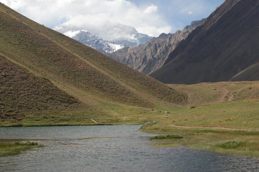 A mountain landscape with a lake, a clear sky, and distant snow-capped peaks. 4