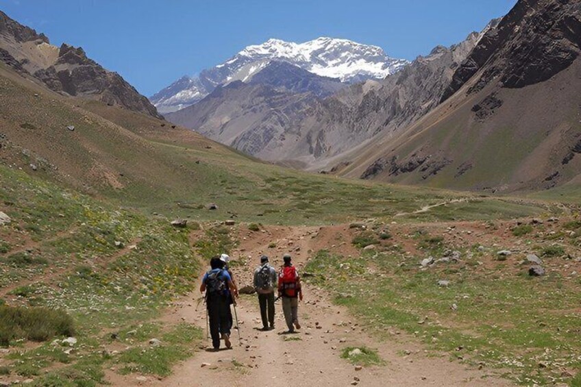 A mountainous landscape with a clear sky, a dirt path, and three hikers. 2