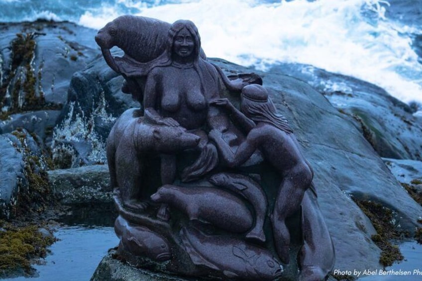 A stone sculpture of a woman and child by a rocky shore. 1