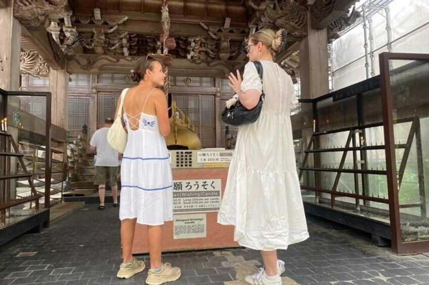 Two people standing in a traditional building with ornate architecture, a sign with Japanese text, and a display case. 3