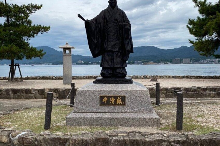 A statue of a historical figure with a plaque, set against a backdrop of water and mountains. 5
