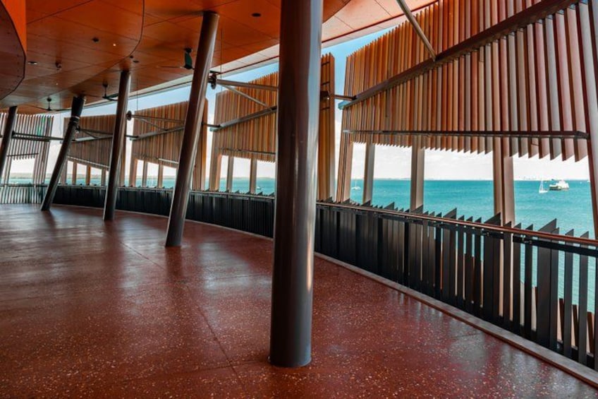 A spacious indoor area with a view of the sea, featuring a wooden slatted ceiling and metal columns. 2