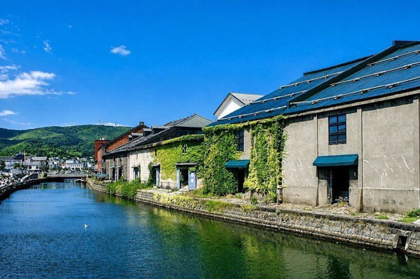 A canal with buildings on one side, a clear blue sky, and a bridge in the distance. 2