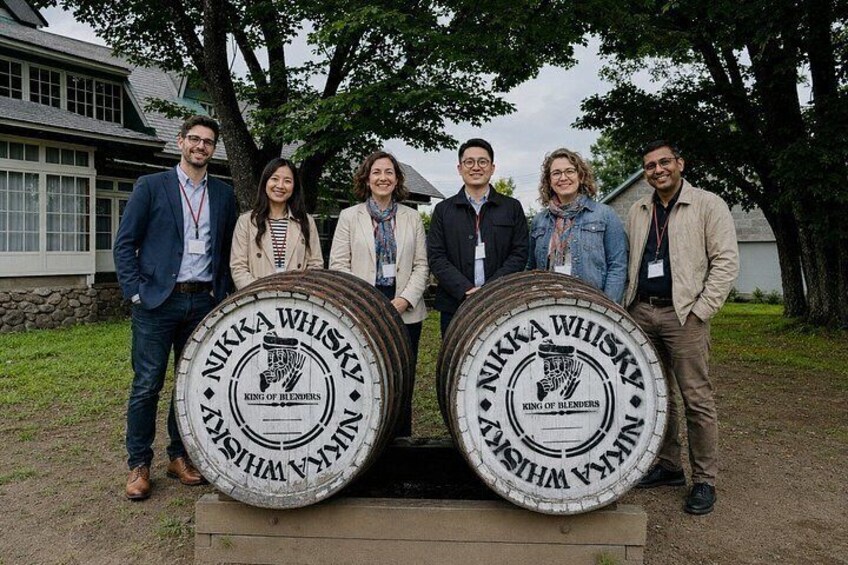 A group of people standing in front of two large barrels with the text 'NIKKA WHISKY KING OF BLENDERS' on them. 1