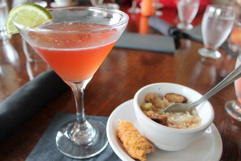 A cocktail glass with a lime garnish, a bowl of rice with chickpeas, and a piece of fried chicken on a table. 3