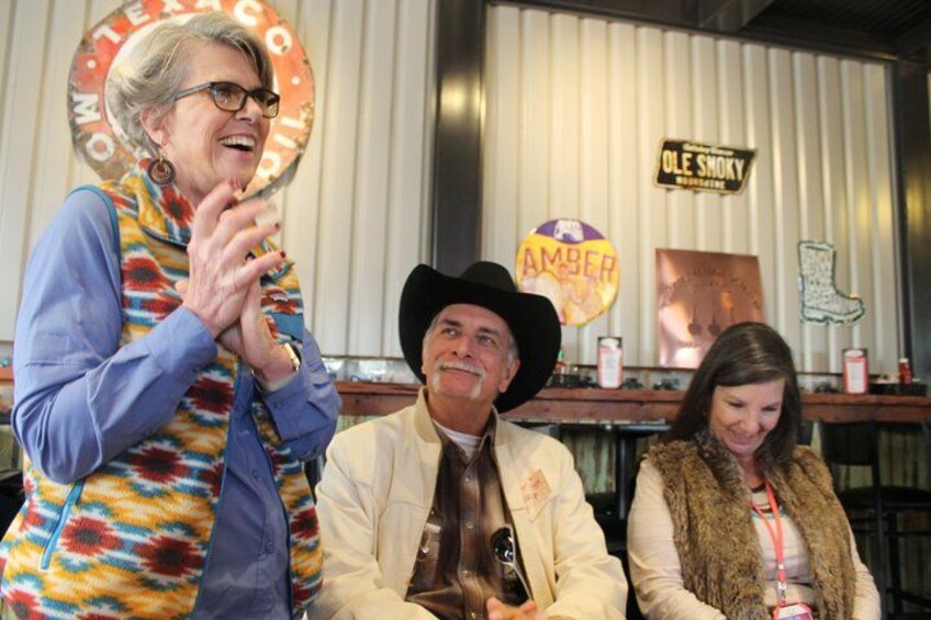 A person in a colorful vest, a person in a cowboy hat, and a person in a fur vest sitting at a bar with a sign that reads 'Ole Smoky.' 5
