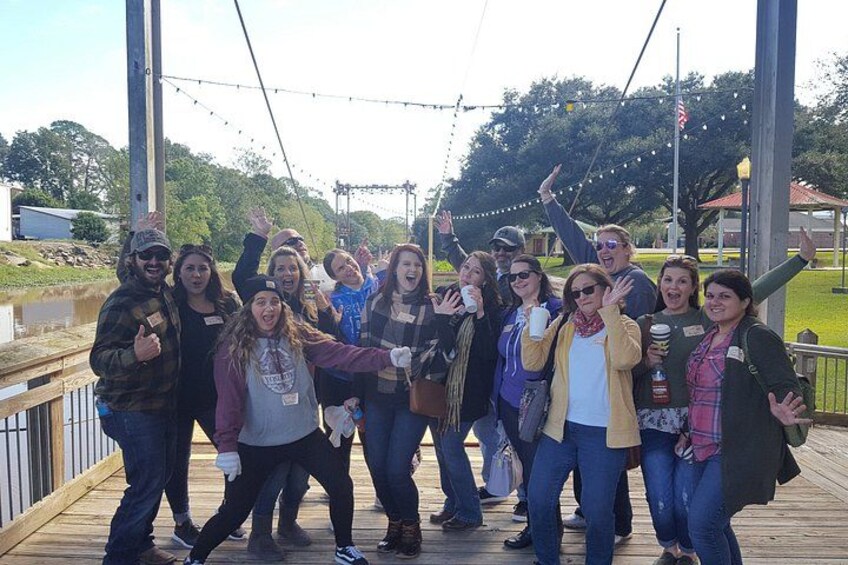 A group of people on a wooden deck with a metal railing, trees, and a building in the background. 3