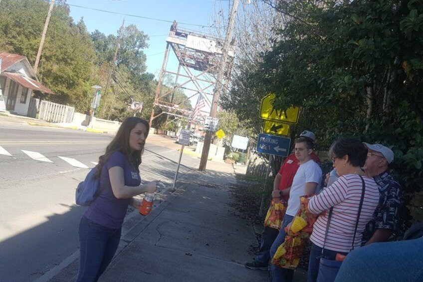 A street scene with a pedestrian crossing sign, a person holding a drink, and a group of people standing on the sidewalk. 2