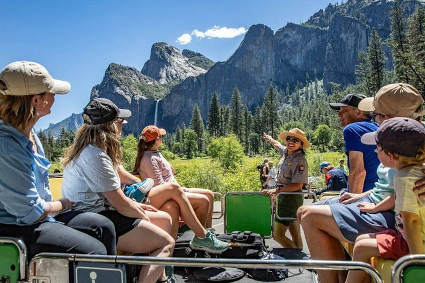 A group of people on a green trolley, enjoying a mountainous landscape with a waterfall and dense forest. 1