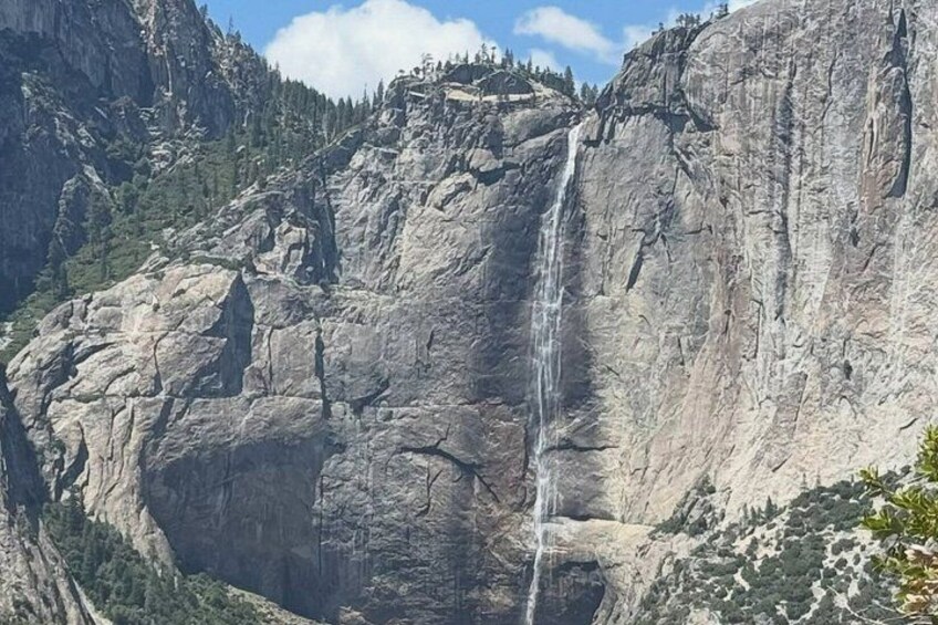 A waterfall cascading down a steep, rocky cliff surrounded by forested mountains. 3