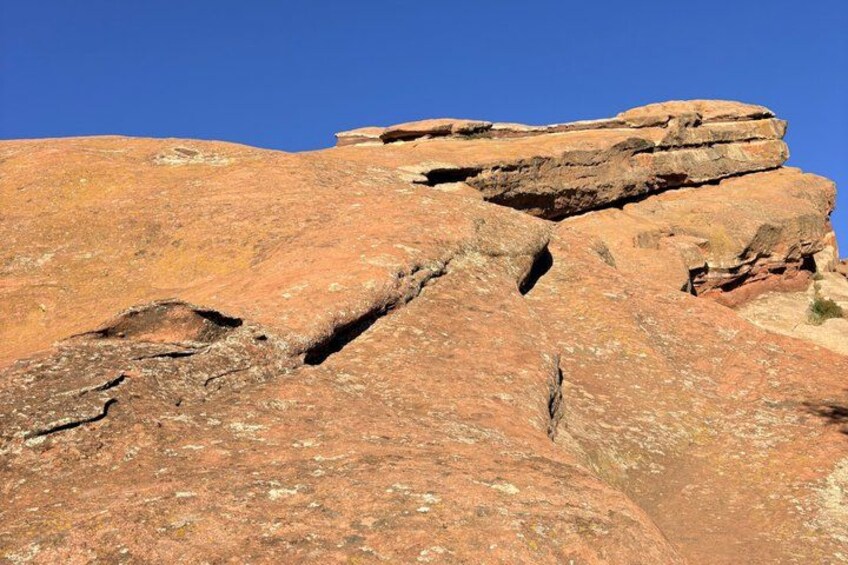 A large reddish-brown rock formation with visible striations and a clear blue sky. 2