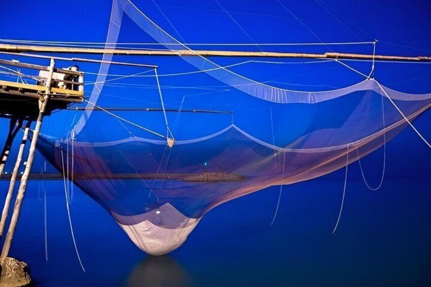 A fishing net suspended over water, a wooden structure, and a clear blue sky. 1